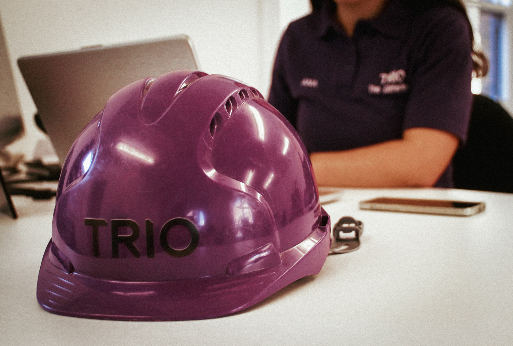 Purple TRIO hard hat on desk with admin team member in background